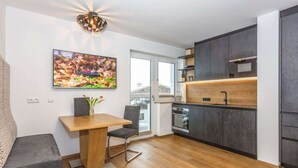 A modern kitchen with dark cabinets, a wooden dining table, and a large window. - Maximilian 1-2 People (Neukirchen am Grossvenediger)
