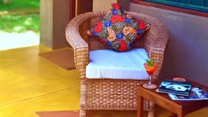 Une chaise en osier avec un coussin coloré et une petite table sur laquelle se trouvent un verre et des magazines.