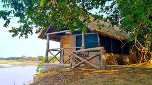 Une cabane rustique en bois, dotée d’un toit de chaume, située au bord d’une rivière paisible.