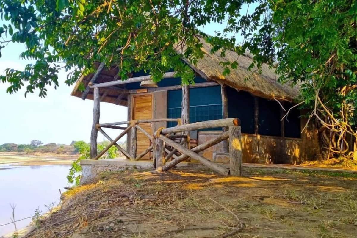 Uma cabana de madeira rústica com telhado de palha, localizada às margens de um rio calmo.