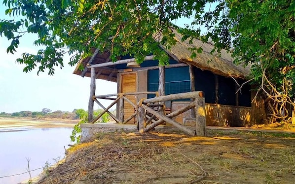 A rustic wooden cabin with a thatched roof, situated by a calm river.