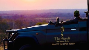 Un véhicule équipé d’un toit ouvrant, portant l’inscription « Thornicroft » et des numéros de téléphone, était garé dans un endroit offrant une vue sur un coucher de soleil se reflétant sur un paysage.