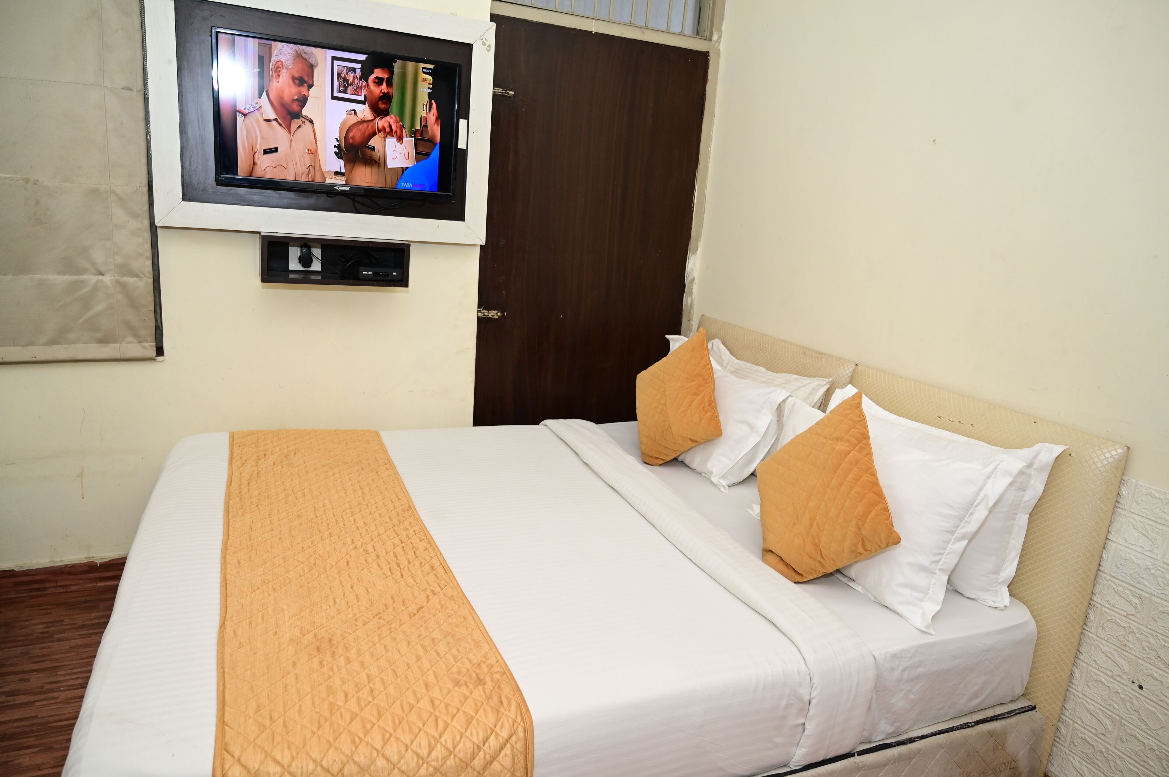 A hotel room with a bed, a television mounted on the wall, and a wooden door.
