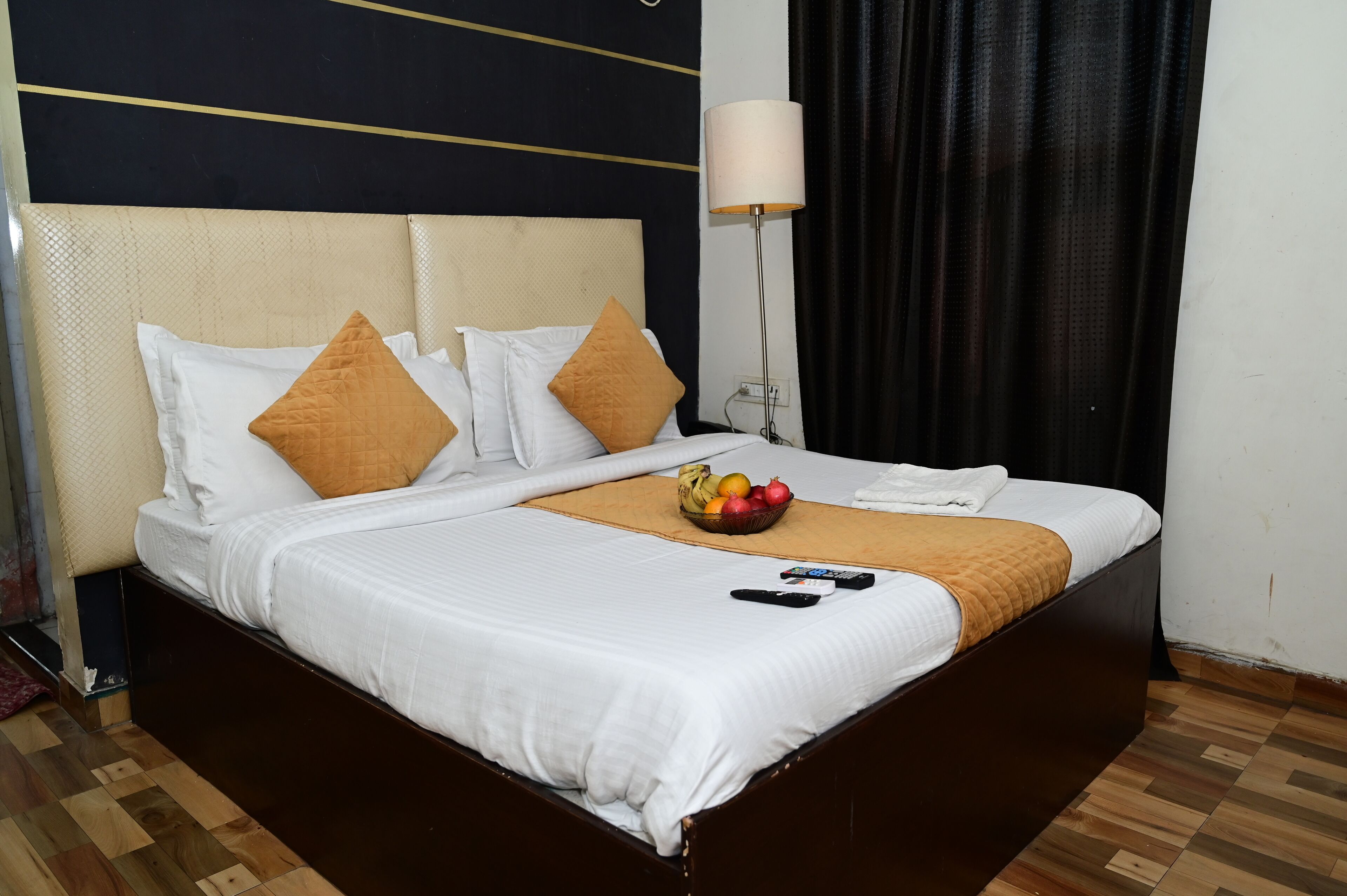 Una cama bien hecha con almohadas blancas y marrones, un frutero y controles remotos sobre la cama.