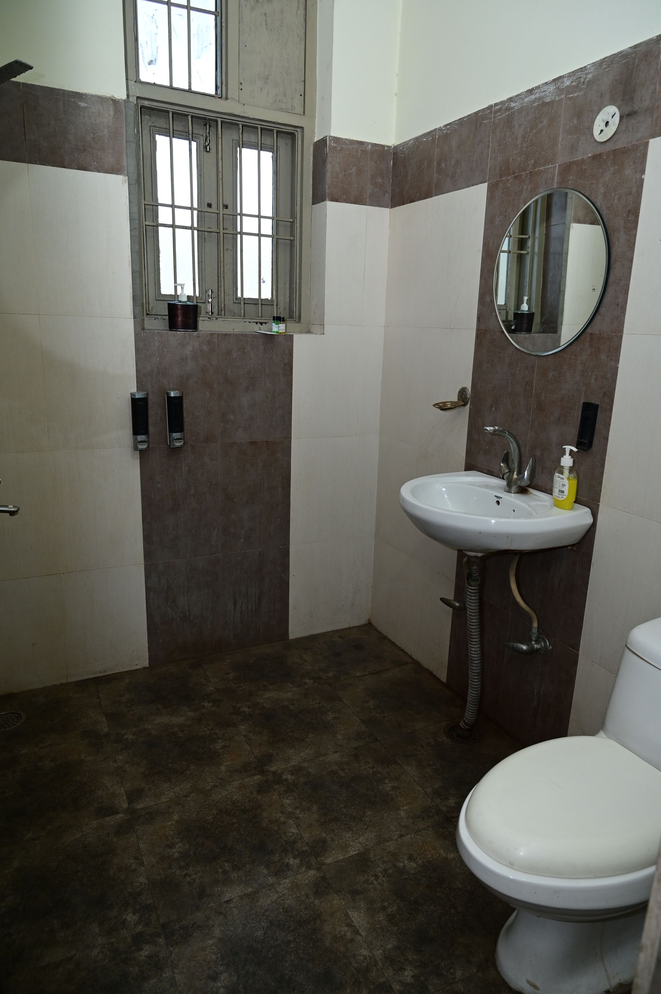 A bathroom with a white sink, a toilet, a mirror, and a window with bars.