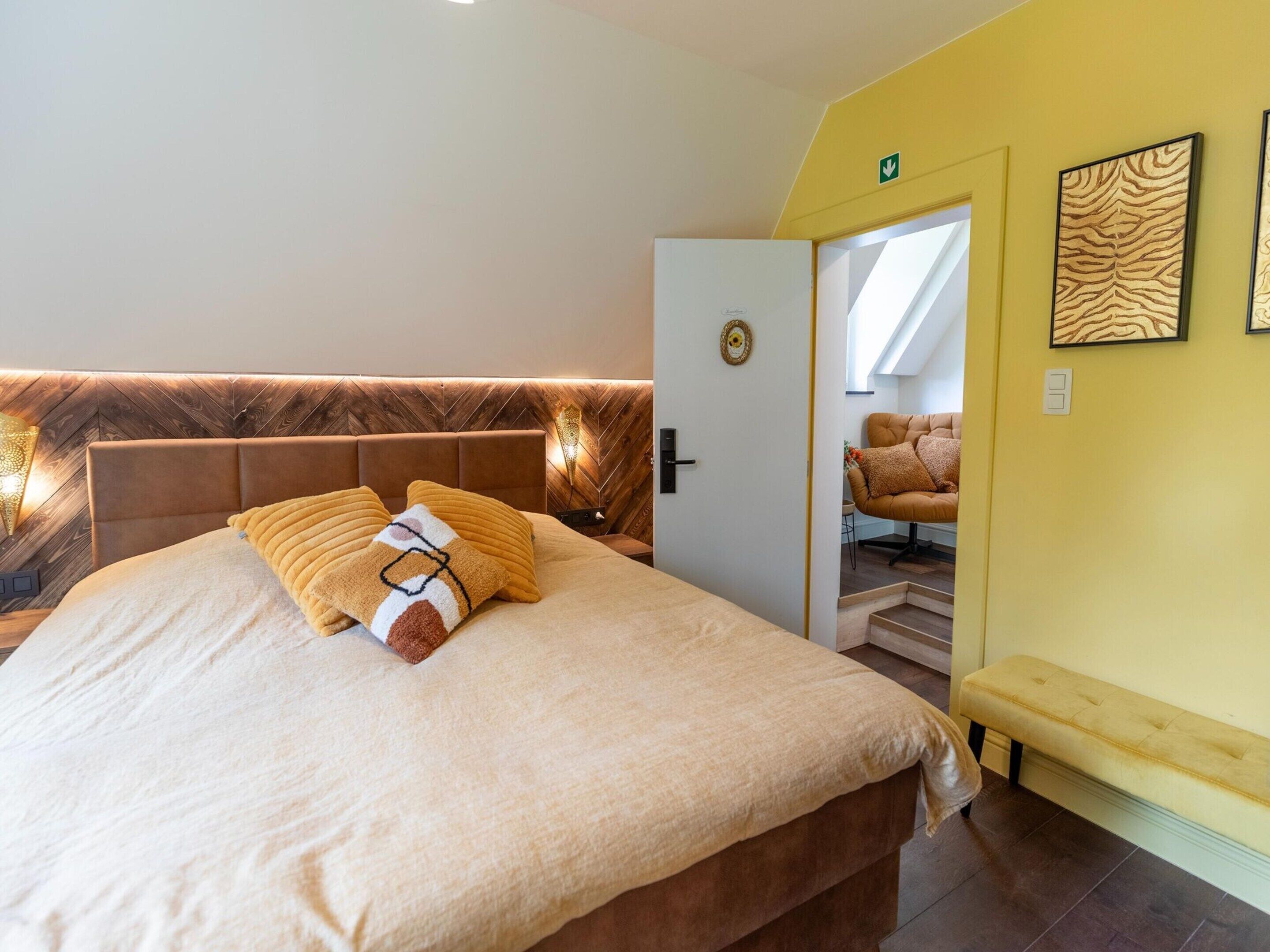 A bedroom with a bed, a bench, a door, and a wall with two framed pictures.