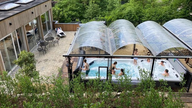 A rooftop pool area with transparent canopies, surrounded by lush greenery and a modern building with large windows. - Luxurious Villa With Heated Pool (Gesves)