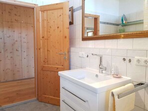 A bathroom with a wooden door, a white sink with a mirror above it, and a towel rack. - Mountain View Comfortable Holiday Residence (Rimsting)