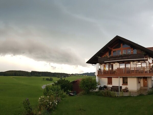 A two-story chalet with a balcony, surrounded by a lush green landscape and a cloudy sky. - Mountain View Comfortable Holiday Residence (Rimsting)