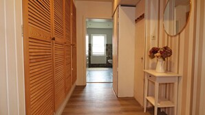 Un couloir avec des portes coulissantes en bois, une console blanche ornée d’un vase de fleurs et un miroir accroché au mur.