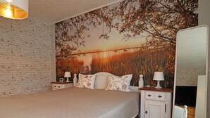 Une chambre avec un mur décoré d’un motif en briques, un lit agrémenté d’oreillers à motifs floraux, une table de chevet avec une lampe et un grand miroir.