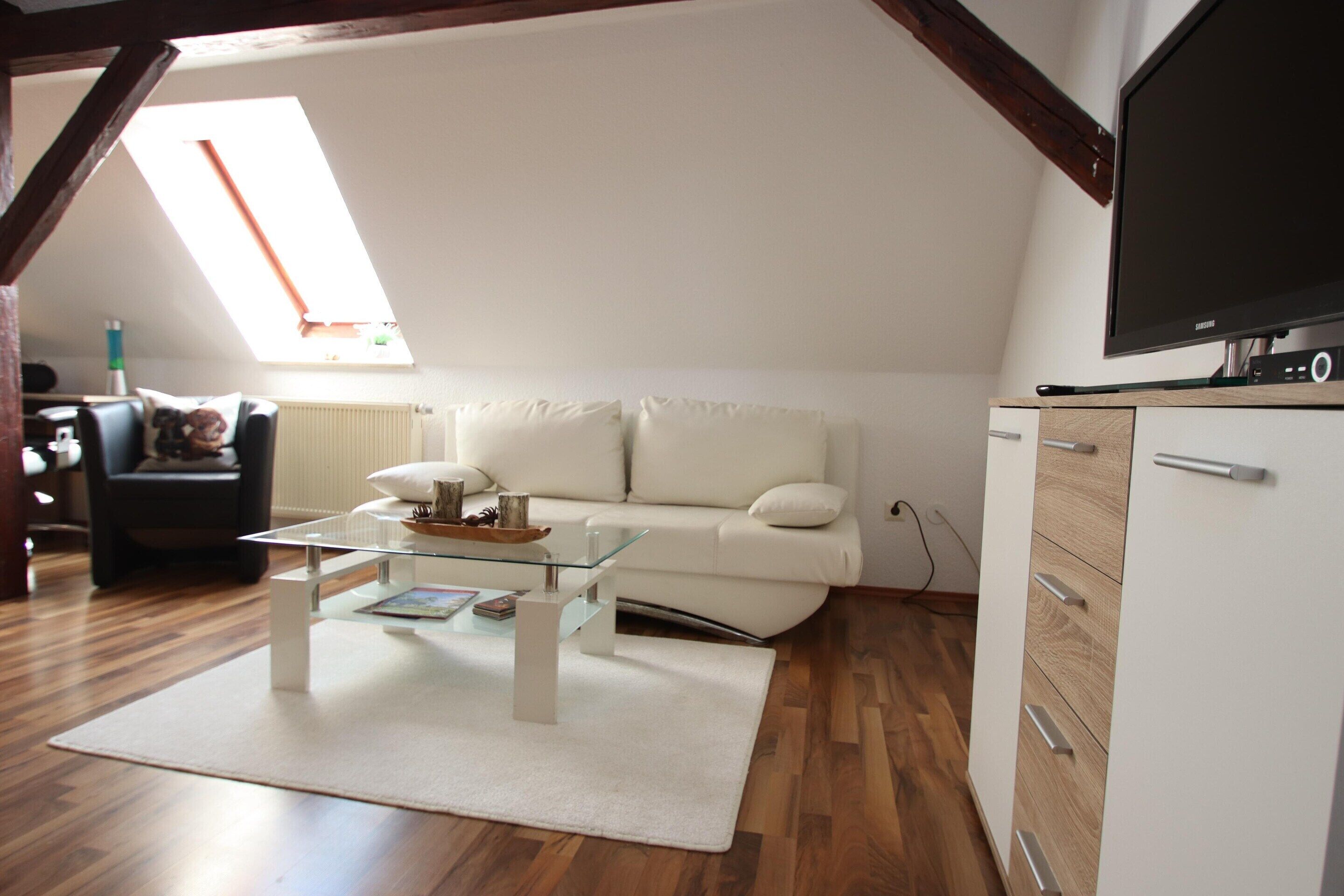 A living room with a white sofa, a glass coffee table, a white cabinet, and a flat-screen TV.