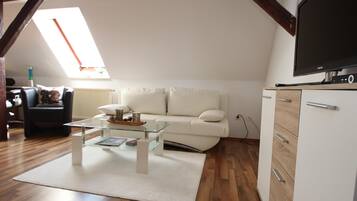 A living room with a white sofa, a glass coffee table, a white cabinet, and a flat-screen TV.
