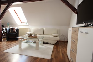 A living room with a white sofa, a glass coffee table, a white cabinet, and a flat-screen TV.