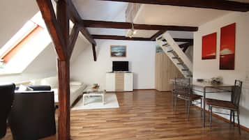 A loft-style living space with exposed wooden beams, a white sofa, a dining table with chairs, and artwork on the walls.