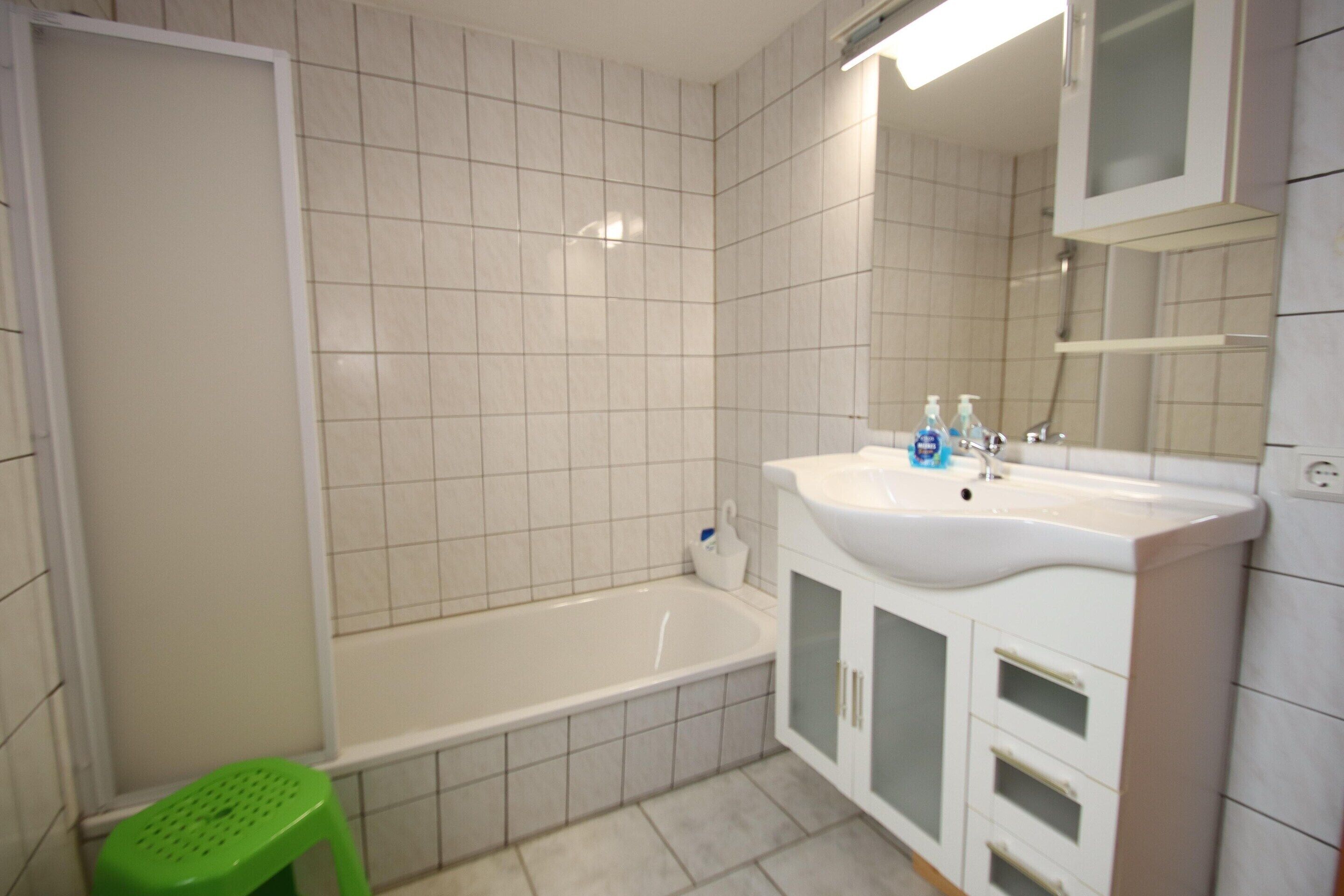 Un baño con bañera, lavamanos, espejo y un taburete verde.