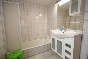 A bathroom with a bathtub, a sink, a mirror, and a green stool.