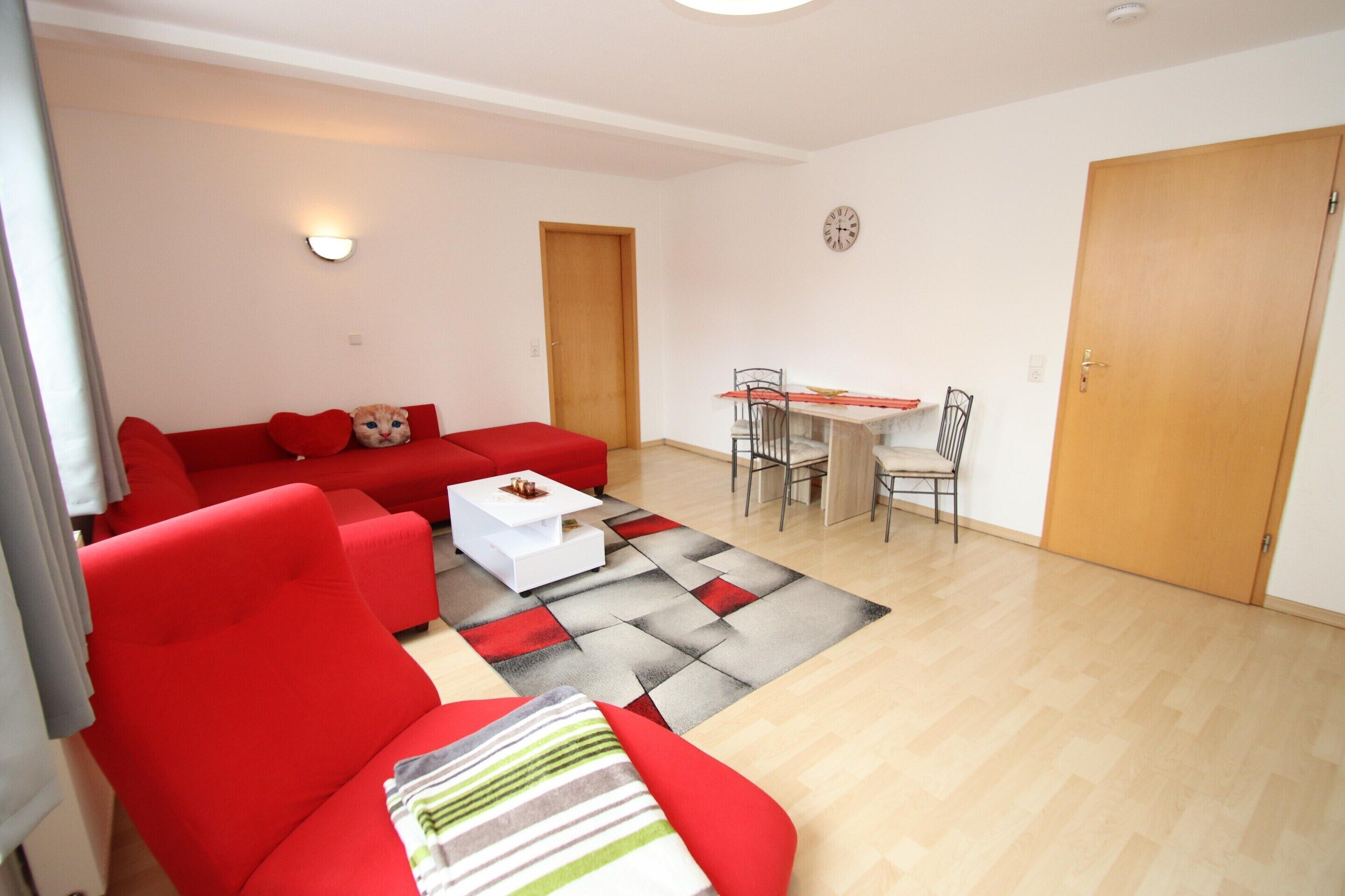 A living room with a red sofa, a white coffee table, and a dining area with a table and chairs.