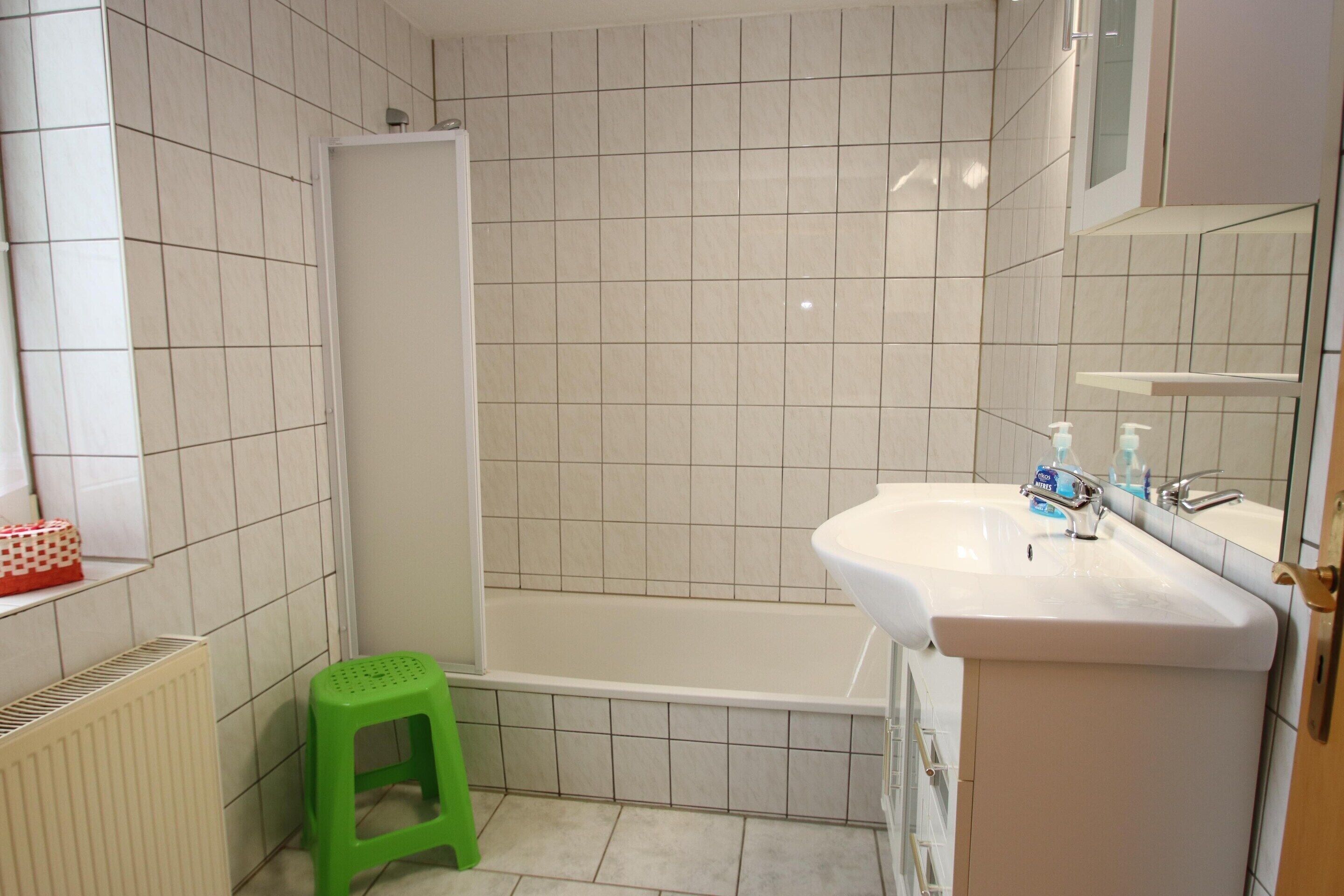A bathroom with a bathtub, a green stool, a white sink, and a mirror.