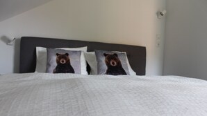 A bed with a white quilt and two pillows featuring a bear design. - Huis 3landenpunt AT-SLO-IT. Holiday in Austria, Slovenia and Italy at once. (Arnoldstein)