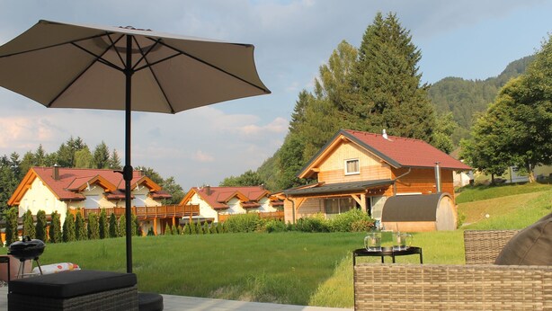 A patio with outdoor furniture, a large umbrella, and a view of a row of houses with red roofs. - Huis 3landenpunt AT-SLO-IT. Holiday in Austria, Slovenia and Italy at once. (Arnoldstein)