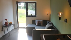 A modern living room with a sofa, a small table, and a window with a view of the outdoors. - Huis 3landenpunt AT-SLO-IT. Holiday in Austria, Slovenia and Italy at once. (Arnoldstein)