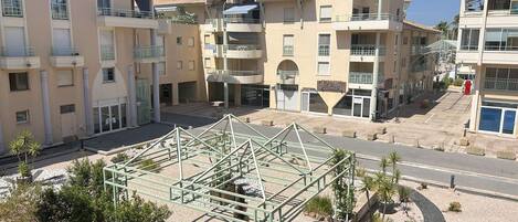 A multi-story residential building with balconies, a central courtyard with a metal structure, and surrounding greenery.