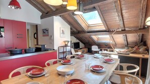 Een eetruimte met een lange houten tafel, gedekt voor vier personen, rode en witte borden en een rode hanglamp erboven.