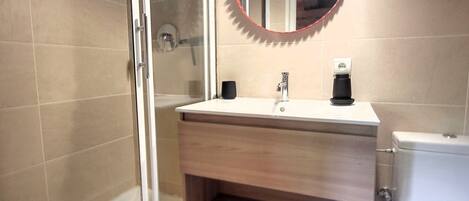 A modern bathroom with a glass shower enclosure, a white sink with a black faucet, and a round mirror with a red frame.