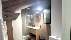 Een moderne badkamer met een douchecabine van glas, een houten wastafelmeubel en een toilet.