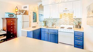 A kitchen with white cabinets, blue drawers, a white stove, and a white refrigerator. - Blue Pearl Oceanfront Modern at Sea Cabin w Pool (North Myrtle Beach)