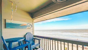 A beachside balcony with a view of the ocean, featuring a wooden chair and a table. - Blue Pearl Oceanfront Modern at Sea Cabin w Pool (North Myrtle Beach)