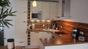 A modern kitchen with white cabinets, a microwave, a coffee maker, and a wooden backsplash. - Coastal Love in Karlshagen (Karlshagen)