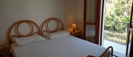 Une chambre à coucher avec un lit, une lampe de chevet, un tableau au mur et une vue sur un balcon doté d’une balustrade.