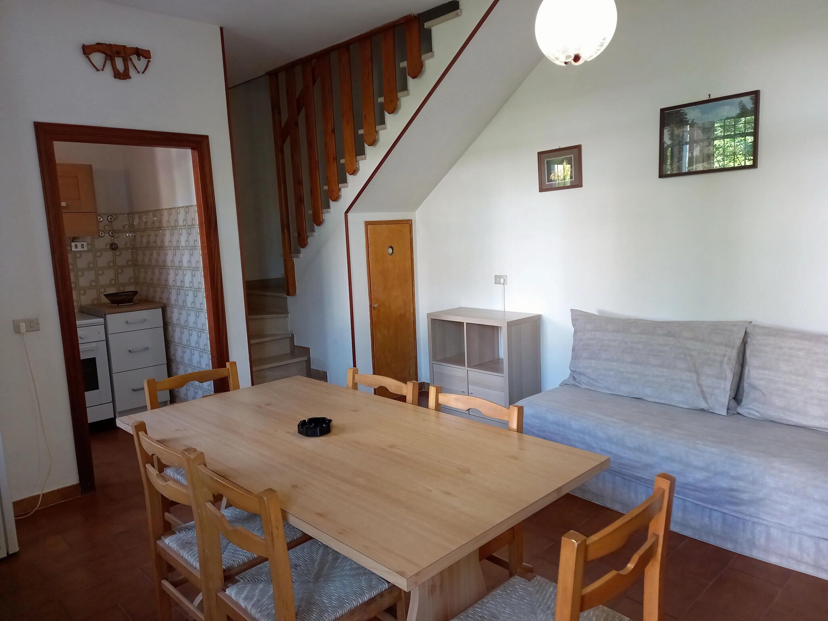 Ein Essbereich mit Holztisch und -stühlen, einer Treppe, einer Couch und einer kleinen Küchenzeile.