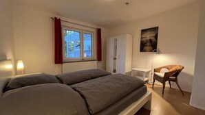 Une chambre à coucher comprenant un lit, un bureau, une chaise, une armoire et une fenêtre avec des rideaux.