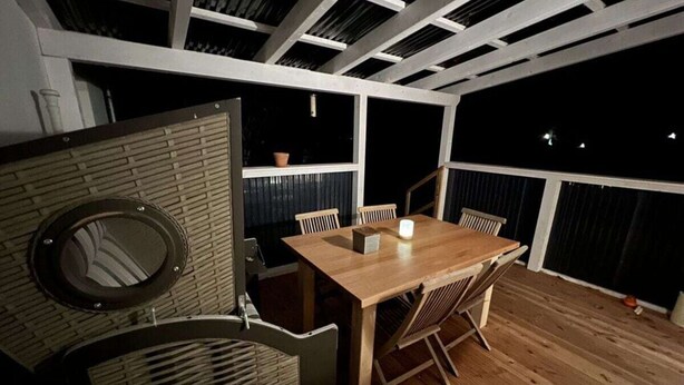 Un espace repas avec une table et des chaises en bois, une plante en pot et une vue sur le ciel nocturne grâce à de grandes fenêtres.