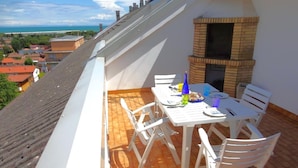 A rooftop terrace with a brick oven, white table and chairs, and a view of the sea. - Apartment in Caorle Near Seabeach (Caorle)