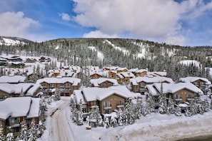 A snow-covered resort with multiple chalet-style buildings, a ski slope in the background, and a clear sky. - Trapper's Landing #39 | 3 Peaks Rentals (Sun Peaks)