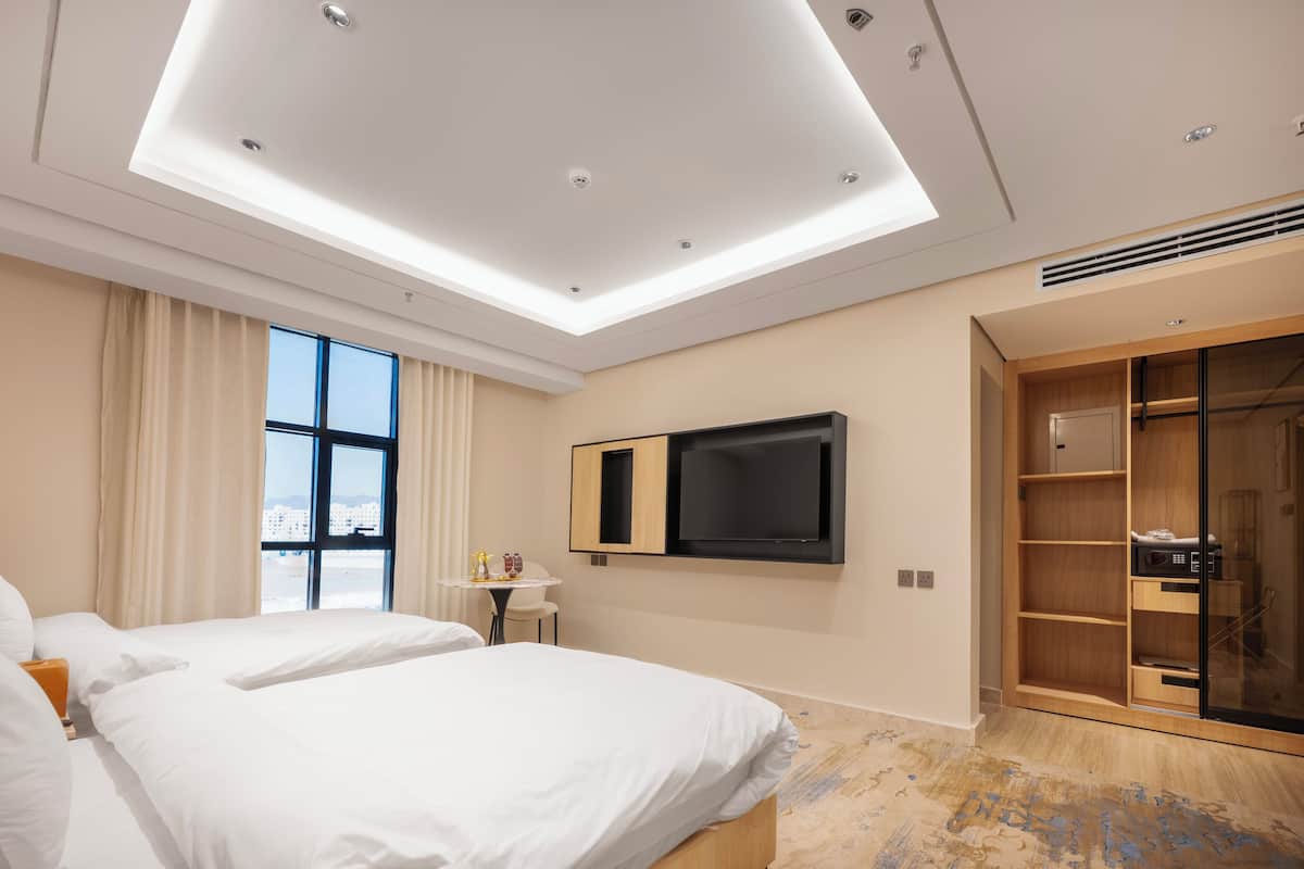 A modern hotel room with two beds, a TV, a desk, and a large wardrobe.
