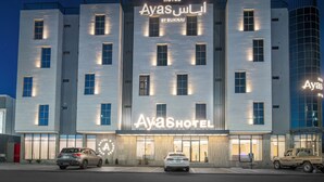 A modern hotel building with illuminated signage, multiple floors, and a parking area with cars. - Ayas Hail Hotel - فندق أياس حائل (Ha'il)