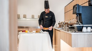 Un chef sirve comida en una cocina moderna con una cafetera y utensilios sobre la encimera.