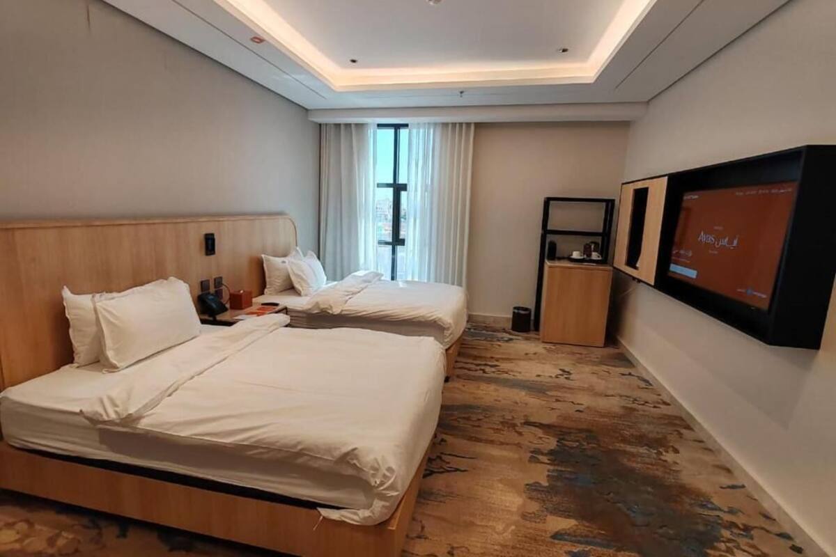 A hotel room with two beds, a television, a small table, and a window with curtains.