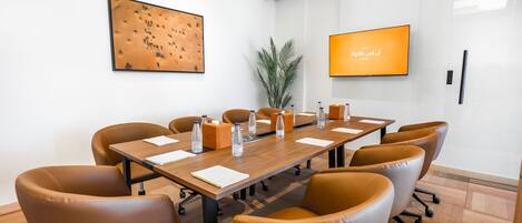 A conference room with a long table, brown leather chairs, water bottles, and a TV screen displaying text.
