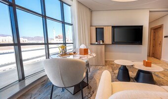 A hotel room with a large window, a flat-screen TV, a marble coffee table, a sofa, and a small side table.