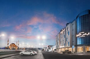A hotel with a modern facade, a prominent sign, and a parking area with vehicles.