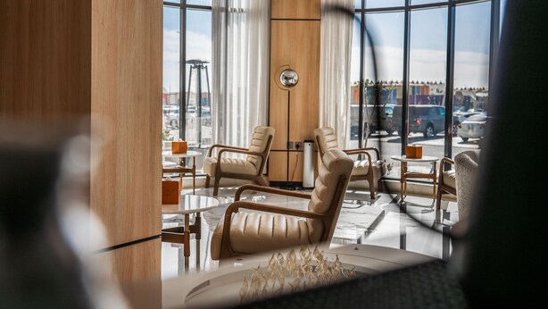Un vestíbulo de hotel moderno con sillones de cuero, una araña y grandes ventanales con vistas a la ciudad.