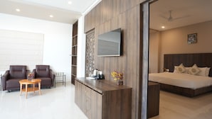 Une chambre moderne avec un grand lit, un téléviseur fixé au mur et un coin salon comprenant un canapé et une petite table.