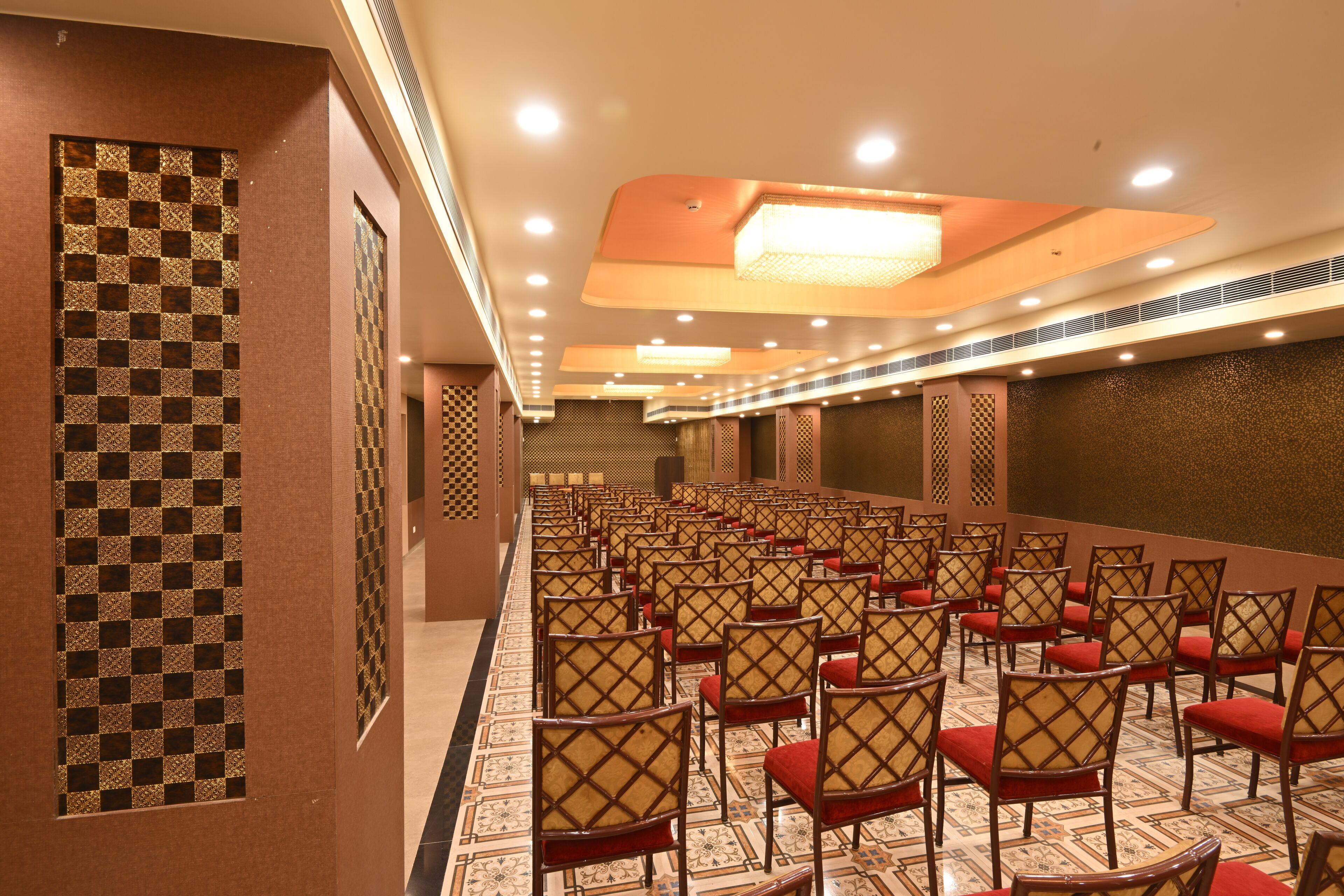 A conference room with rows of chairs, a patterned wall, and a ceiling with recessed lighting.