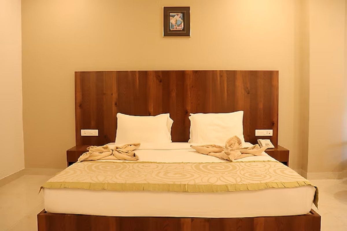 Ein ordentlich bezogenes Bett mit Holz-Kopfteil, weißen Kissen und einer beige farbenen Bettdecke. Zwei Nachttische mit Lampen und ein kleines gerahmtes Bild an der Wand über dem Bett.